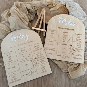 Può includere: Due cartelli in legno con la parte superiore arrotondata, decorati con un arco bianco e i nomi "Haley" e "Mila". I cartelli sono decorati con illustrazioni di un coniglio, un dinosauro e un dente. I cartelli elencano informazioni sui primi compleanni dei bambini, tra cui le loro date di nascita, i loro pesi, le loro altezze e i loro cibi preferiti.