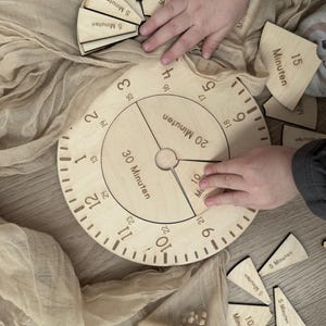 Könnte beinhalten: Ein Holz-Zifferblatt mit den Zahlen 1 bis 12 und Markierungen für 5, 10, 15, 20 und 30 Minuten. Das Zifferblatt ist von Holzstücken umgeben, auf denen die Wörter "5 Minuten", "10 Minuten" und "15 Minuten" stehen.