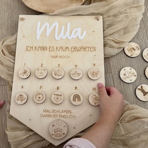 May include: Wooden countdown calendar with the name "Mila" in white. The calendar has ten numbered wooden discs with animal and object illustrations. The text "ICH KANN ES KAUM ERWARTEN" and "MAL SCHLAFEN, DANN IST ENDLICH" are also visible.