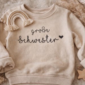 Könnte beinhalten: Drei cremefarbene Keramikbecher mit gesprenkelter Glasur. Jeder Becher zeigt ein handgemaltes Blumenmuster in Blau, Grün und Gelb. Die Becher haben eine einfache, abgerundete Form und einen Henkel.