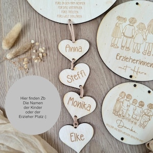 May include: Wooden heart-shaped tags with the names Anna, Steffi, Monika, and Elke. The tags are hanging from a string. The text "Hier finden Zb Die Namen der Kinder oder der Erzieher Platz :" is visible on a wooden surface.