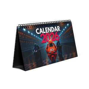 Puede incluir: Un calendario de escritorio para 2026 con temática de carreras. La portada muestra tres motocicletas compitiendo en una pista, con la palabra "CALENDAR" sobre el año "2026". El calendario está encuadernado con una espiral negra.