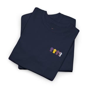 May include: Two navy blue t-shirts are folded and stacked. Each shirt has a small embroidered design of colorful jerseys on the left chest. The jerseys are in various colors, including blue, yellow, red, and white.