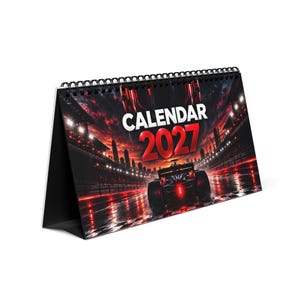 Peut inclure: Un calendrier de bureau pour l'année 2027 avec une reliure spirale noire. La couverture présente une illustration graphique d'une voiture de course sur une piste de nuit, avec des tons rouges et noirs, des lumières de ville et le texte CALENDAR 2027.