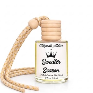 May include: A small, clear glass bottle with a wooden cap and a beige cord. The label reads "Sweater Season" with a crown graphic. The bottle contains .27 oz / 8 ml of liquid.