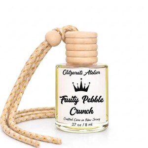 May include: A small clear glass bottle containing yellow liquid with a light wooden cap and a beige braided hanging cord. The label features the text Glitzarati Atelier, a crown icon, and the words Fruity Pebble Crunch, .27 oz / 8 ml.