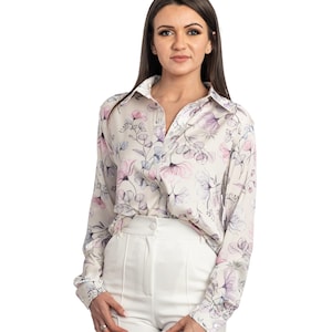 May include: A white long-sleeved blouse with a floral print in shades of pink, purple, and blue. The blouse has a button-down front and a collar.