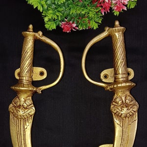 以下が含まれることがあります： 複雑なディテールが施された剣の形をした、装飾的な真鍮製のドアノブのペア。ノブは金色の仕上げで、伝統的なインドの武器に似せて作られています。