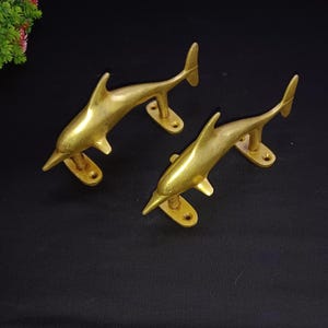 Puede incluir: Dos tiradores de puerta en forma de delfín dorados. Los tiradores están hechos de latón macizo y tienen un acabado pulido.