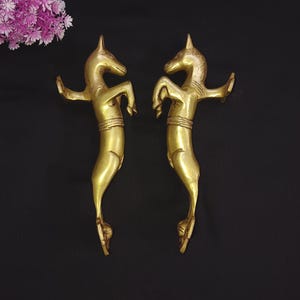 May include: A pair of gold-toned metal door handles shaped like rearing horses. The handles are detailed with intricate carvings and have a polished finish.