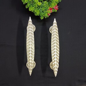 Könnte beinhalten: Zwei silberne, blattartige Türgriffe mit einem Chevron-Muster. Die Griffe sind für die Verwendung an Türen konzipiert.