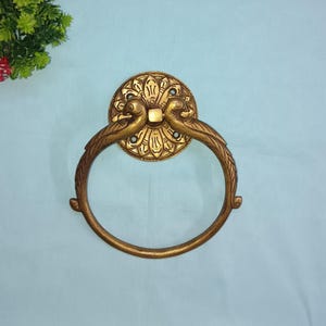 Può includere: Un anello porta asciugamani in metallo dorato con un design decorativo che presenta due uccelli e un motivo floreale. L'anello è di forma ovale e ha una finitura liscia.