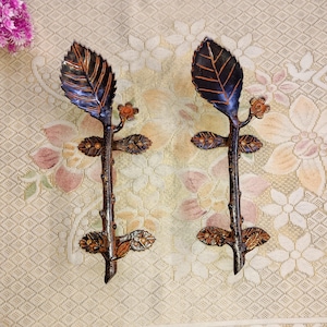 May include: A pair of decorative door handles with a leaf and branch design. The handles are made of metal and have a rustic brown finish.