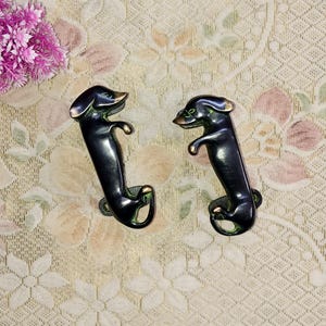 Può includere: Due maniglie per porte a forma di bassotto nero con finitura patina verde.