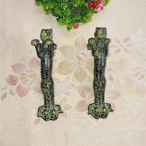 Puede incluir: Un par de tiradores de puerta decorativos con forma de tigres. Los tiradores están hechos de latón y tienen un acabado de pátina verde. Los tigres están de pie sobre sus patas traseras con las patas levantadas.