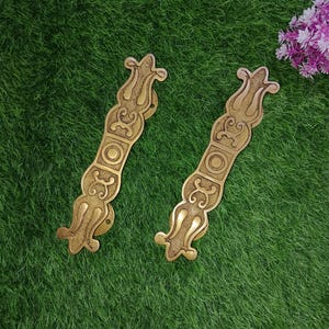 May include: Two ornate brass door handles with intricate floral designs. The handles are a warm gold color and have a smooth, polished finish.