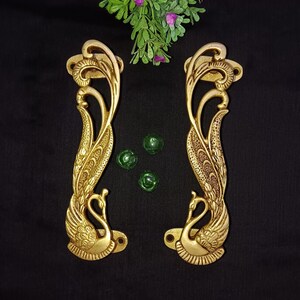 May include: A pair of ornate gold-toned door handles shaped like peacocks with intricate details. The handles are made of metal and have a traditional design.