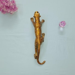 Peut inclure: Une poignée de porte en métal de couleur dorée en forme de léopard. La poignée est détaillée avec des taches et a une finition texturée.