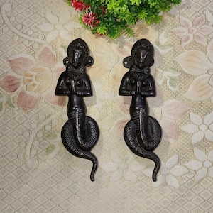 May include: A pair of black metal door handles shaped like a woman with a snake tail. The handles are in a praying position with their hands clasped together.