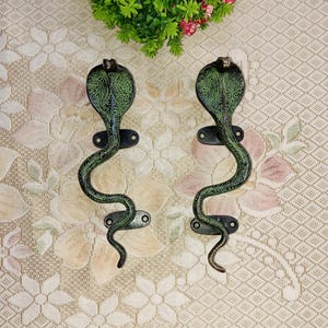 May include: A pair of decorative door handles shaped like green snakes with intricate patterns. The handles are made of metal and have a dark brown finish.
