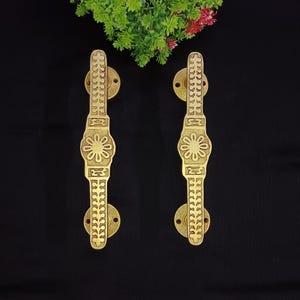 May include: A pair of gold door handles with intricate floral and geometric designs. The handles are made of brass and have a polished finish.