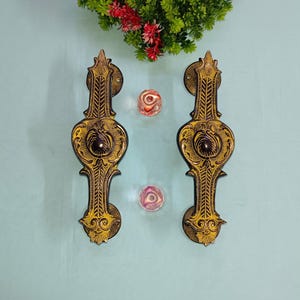 May include: A pair of ornate door handles with intricate designs. The handles are made of brass and have a black finish with gold accents. The handles are in the shape of a heart with a decorative design.