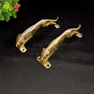 Può includere: Due maniglie per porte in metallo dorato a forma di tigri che saltano. Le maniglie sono dettagliate con pelliccia testurizzata e hanno una finitura lucida.