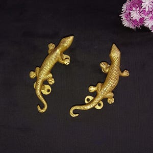 May include: Two gold-toned metal lizard door handles. The lizards are facing opposite directions and have detailed scales.