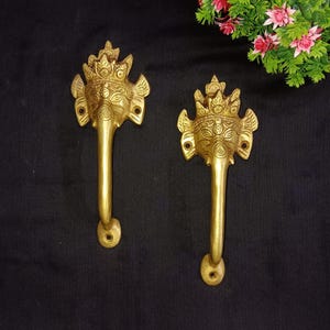 May include: A pair of gold-toned door handles with intricate designs featuring a face with a crown and wings. The handles are made of brass and have a long, curved shape.
