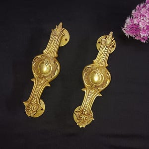 May include: Two ornate gold door handles with intricate floral designs. The handles are made of brass and have a polished finish.