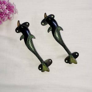 May include: Two black and green dolphin shaped door handles with a brass finish.