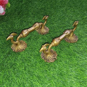 May include: Two ornate brass door handles shaped like peacocks with their tails fanned out. The handles are a gold color and have intricate details.