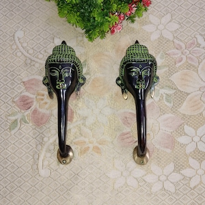 Op de afbeelding: Een paar zwarte en groene deurgrepen met een Boeddha-gezichtsontwerp. De grepen zijn van metaal en hebben een traditionele stijl.