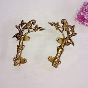 Op de afbeelding: Een paar gouden metalen deurgrepen in de vorm van een boom met een papegaai die op een tak zit. De grepen hebben een gedetailleerd ontwerp en zijn perfect om elke kamer een vleugje natuur te geven.