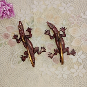 May include: Two red metal lizard wall hooks with gold accents. The lizards are facing opposite directions and have their tails curled up.
