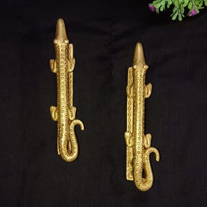 May include: Two gold-toned alligator-shaped door handles with a textured surface.