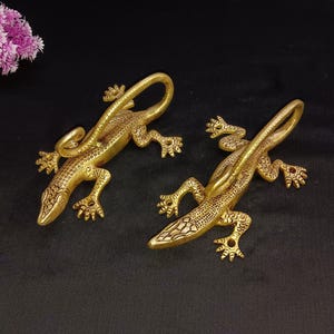 May include: Two gold-colored lizard-shaped wall hooks. The lizards are detailed with scales and have curled tails.