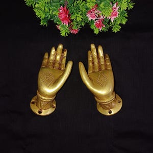 Può includere: Un paio di maniglie per porte in metallo dorato a forma di mani con disegni intricati. Le maniglie sono montate su una base rotonda con fori per viti.