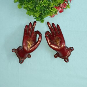 Peut inclure: Une paire de poignées de porte en métal rouge en forme de mains dans un geste de bénédiction. Les mains ont des accents dorés et des détails complexes.