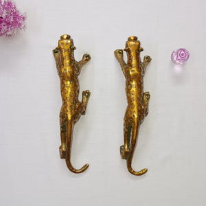 Peut inclure: Deux poignées de porte en métal doré en forme de léopard. Les poignées sont détaillées avec un motif léopard et ont une forme incurvée.