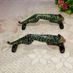 Peut inclure: Deux poignées de porte en métal noir et vert en forme de léopard courant. Les poignées ont un design détaillé avec des accents verts.
