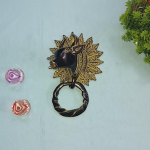 以下が含まれることがあります： 牛の頭のデザインが施された金色と黒色のドアノッカー。牛の頭は黒く、周囲のデザインは金色です。