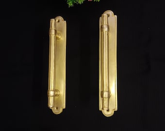 May include: Two gold-toned door handles with a rectangular shape and a long, cylindrical pull. The handles have a decorative design around the edges.