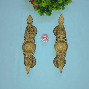 May include: Two ornate door handles with intricate black and gold designs. The handles are made of wood and have a traditional style.