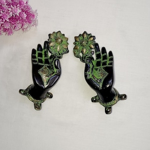 Puede incluir: Un par de tiradores de puerta de metal negro y verde con forma de manos que sostienen una flor. Los tiradores tienen detalles intrincados y un diseño tradicional.