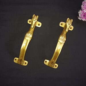 Könnte beinhalten: Zwei goldfarbene Türklinken mit einem Pferdedesign. Die Griffe sind aus Metall und haben eine polierte Oberfläche.