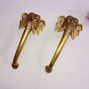 Könnte beinhalten: Zwei goldfarbene Türgriffe in Form von Elefantenköpfen mit aufwendigen Details. Die Griffe sind aus Metall und haben eine polierte Oberfläche.