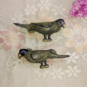 May include: Two black metal parrot door handles with gold accents. The parrots are facing opposite directions and have detailed carvings.