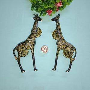 Peut inclure: Deux figurines de girafe en métal noir et jaune. Les girafes sont debout sur une surface bleu clair.