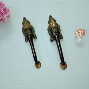 Peut inclure: Deux poignées de porte ornées de noir et de vert avec un motif de visage. Les poignées sont en métal et ont un style indien traditionnel.